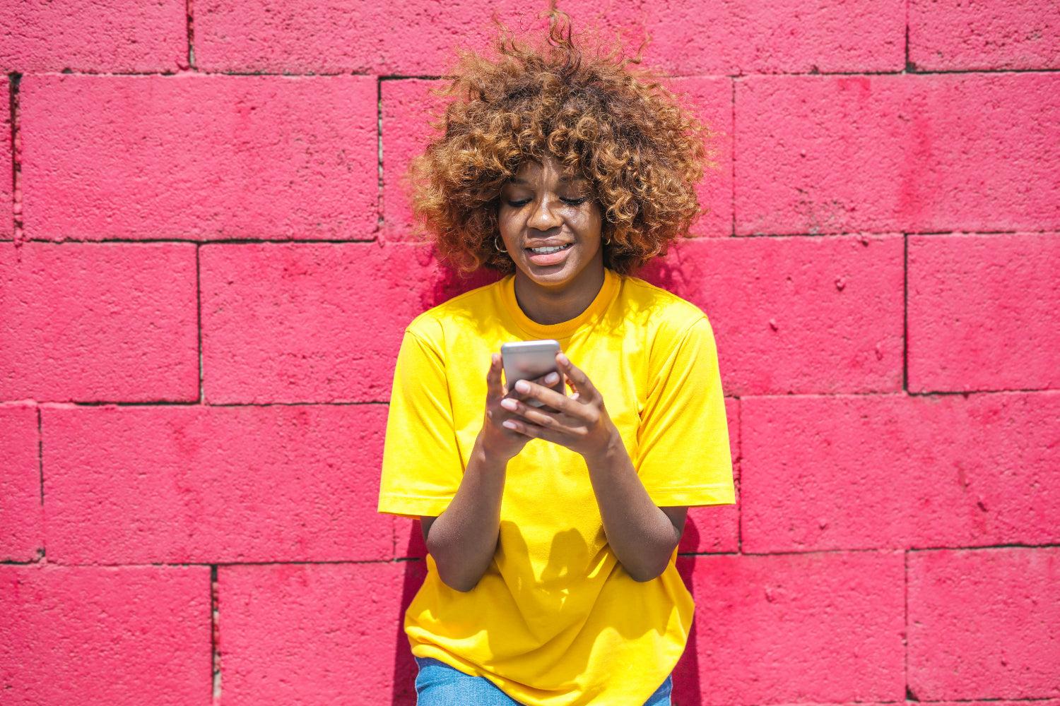 A woman leans on a pink brick wall using her phone